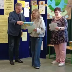 Nagroda za matematyczne zadanie "Kształty na talerzu". Uczennica odbiera pudełko, nauczyciel wręcza dyplom. Funkcja poetycka w nauce.