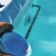 Dłoń wsypuje granulki bromu do błękitnej wody jacuzzi, dbając o czystość.