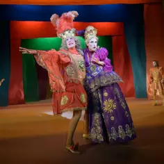 Aktorzy w barwnych strojach, niczym z komedii Moliera, pozują na scenie.