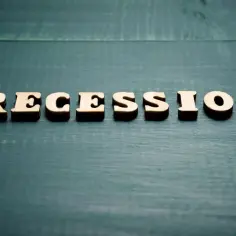 Drewniane litery układają słowo "RECESSION" na ciemnozielonym, drewnianym tle. Nadchodzi recesja.