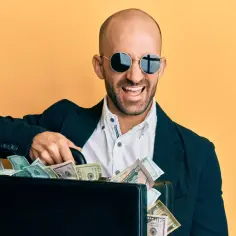 Uśmiechnięty mężczyzna w okularach przeciwsłonecznych trzyma walizkę pełną pieniędzy, jakby symbolizującą przypowieść o talentach i ich pomnażaniu.