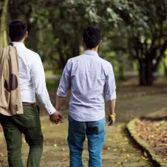 Dwóch mężczyzn idzie ręka w rękę po ścieżce w parku. Ich homoseksualizm jest widoczny w ich bliskości.