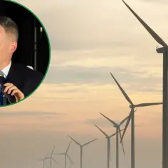 Mężczyzna w garniturze przemawia na tle farmy wiatrowej, symbolizującej przyszłość energii wiatru.