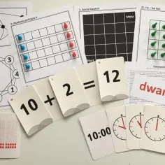 Zestaw kart edukacyjnych z cyframi, zegarami i zadaniami matematycznymi, w tym plansza z pionkami i schemat ośmiokąta. To świetny **organizm** do nauki.