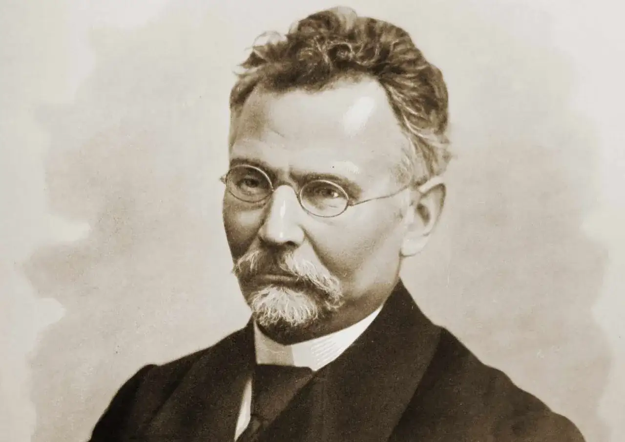 Portret mężczyzny w okularach, z wąsami i brodą. Jego twarz przypomina nieco postać z 