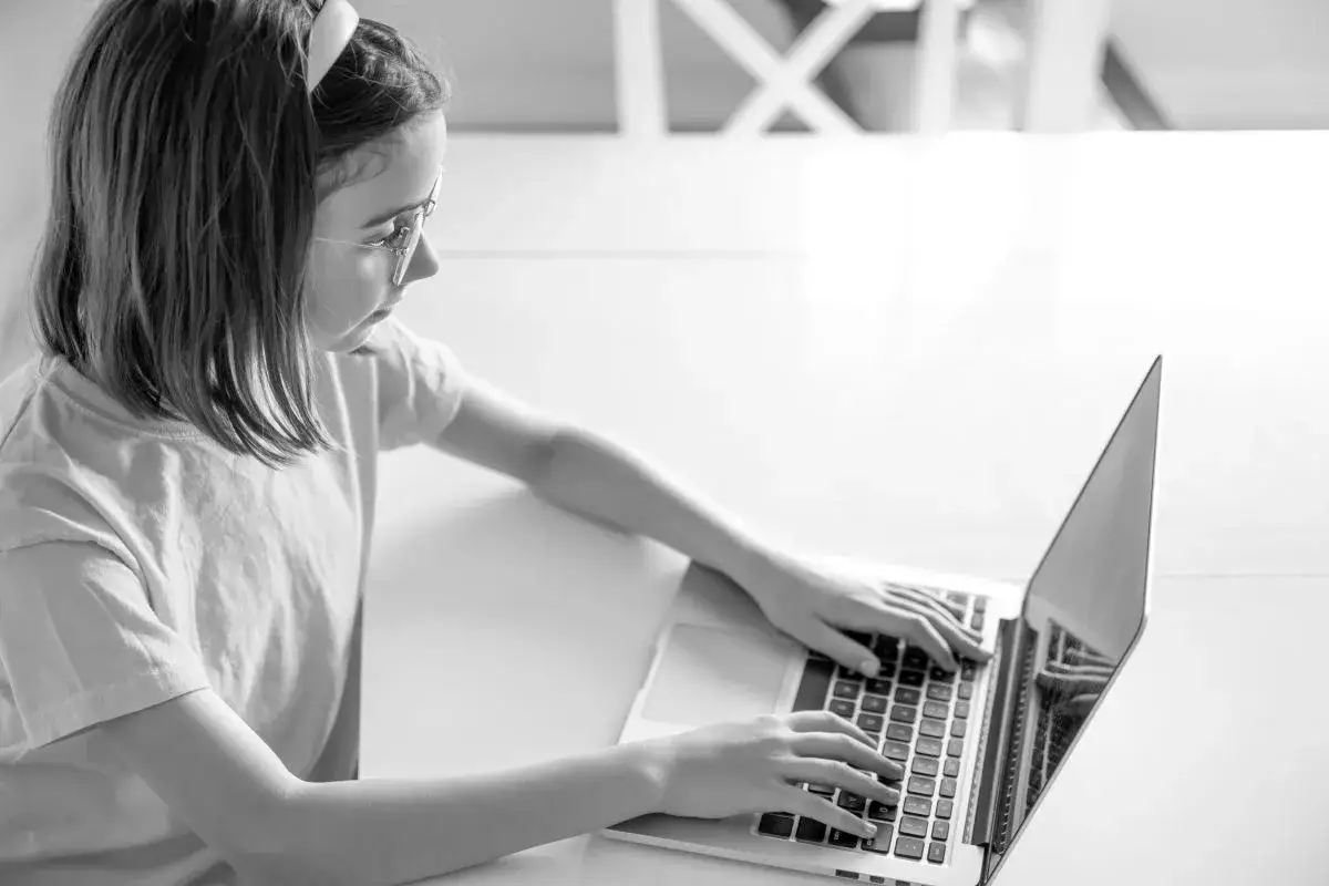 Dziewczynka w okularach uczy się o bezpieczeństwie w internecie, pisząc na laptopie.