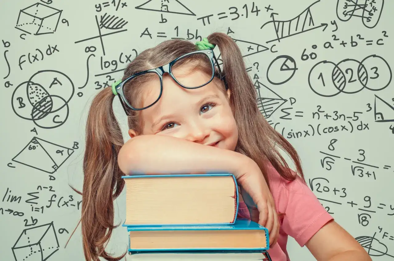 Uśmiechnięta dziewczynka w okularach opiera się o stos książek na tle tablicy z matematycznymi wzorami. Jej oczy błyszczą, a na twarzy maluje się radość odkrywania. To dziecko zafascynowane funkcjami językowymi matematyki.