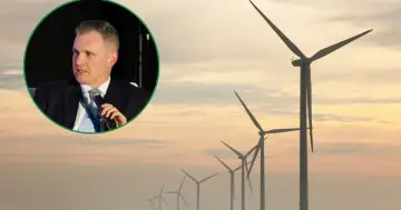 Mężczyzna w garniturze przemawia na tle farmy wiatrowej, symbolizującej przyszłość energii wiatru.