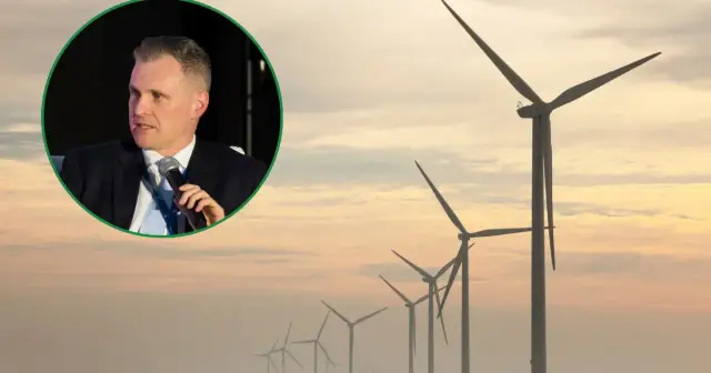 Mężczyzna w garniturze przemawia na tle farmy wiatrowej, symbolizującej przyszłość energii wiatru.